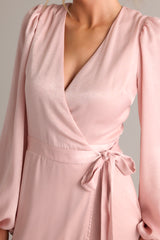 Close up view of this dusty pink wrap dress featuring a v-neckline, balloon sleeves, an adjustable tie around the waist, and an asymmetrical flowy skirt.