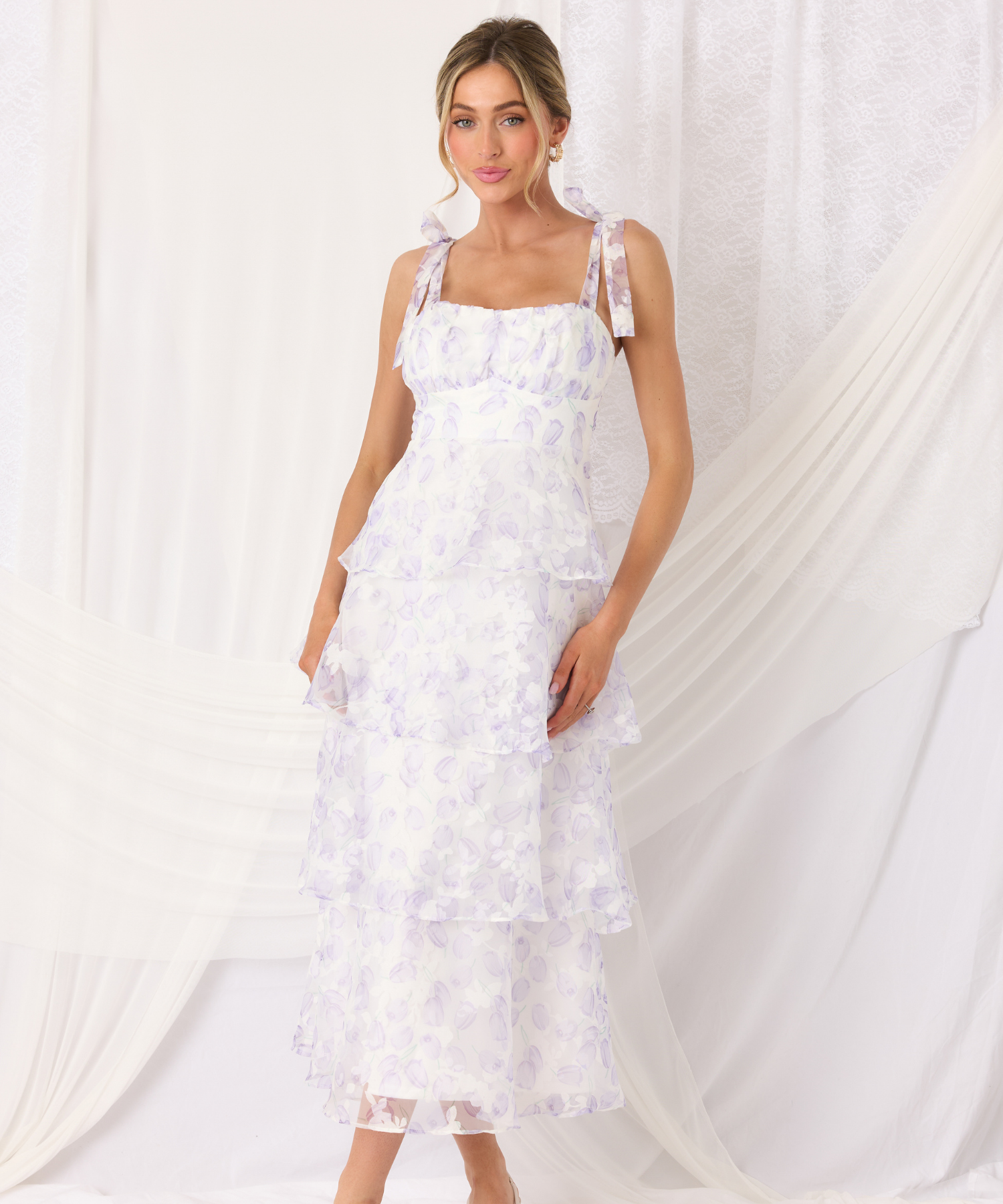 Woman wearing a white floral dress against a white curtain background