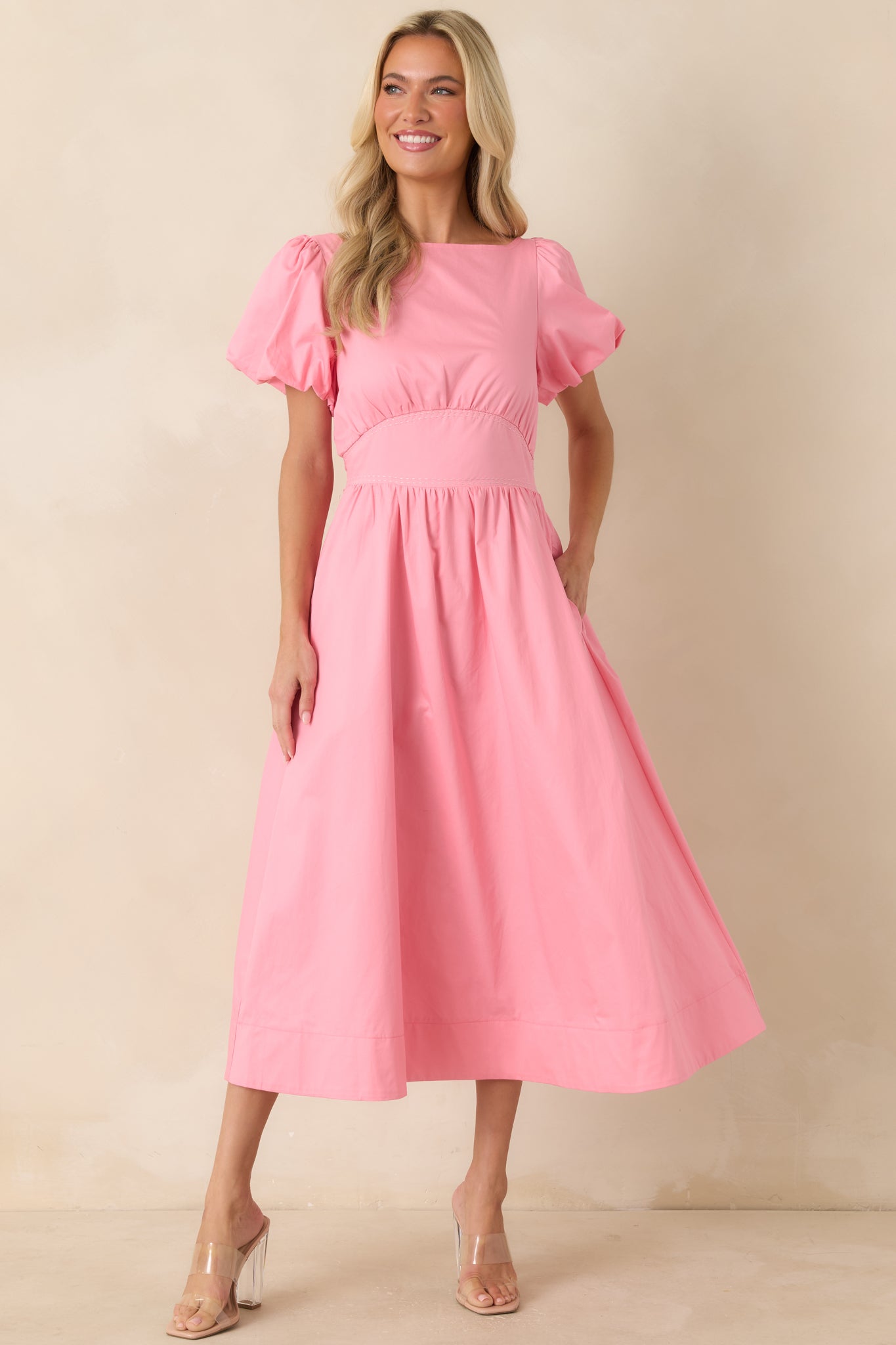 Pink lined midi dress featuring puff sleeves, side pockets, and a flattering fitted waist with subtle contrast stitching.