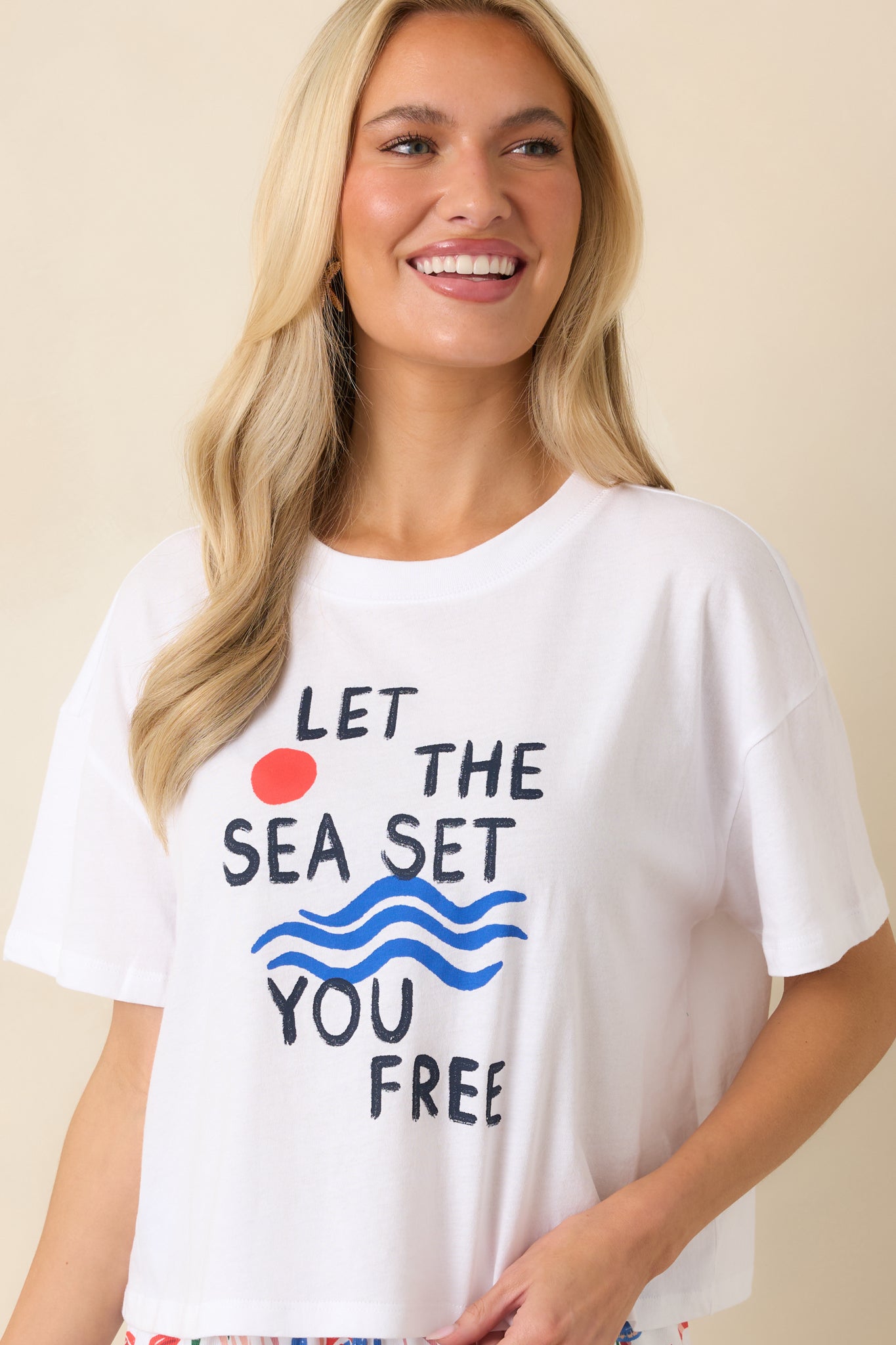 Cropped front view of the white cotton tee showcasing the “Let the Sea Set You Free” graphic with sun and wave illustrations.