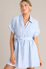 Full front view of  this dress that features a collared v-neckline, a full button front, an elastic waistband, a self-tie belt, functional pockets, and folded sleeves.