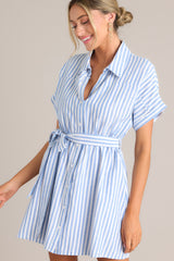 Front view of  this dress that features a collared v-neckline, a full button front, an elastic waistband, a self-tie belt, functional pockets, and folded sleeves.