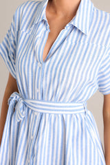 Close up view of this dress that features a collared v-neckline, a full button front, an elastic waistband, a self-tie belt, functional pockets, and folded sleeves.