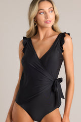 Front view of this black swimsuit that features a deep v-neckline, a shelf bra, removable padding, ruffled shoulders, a self-tie wrap style design, and an open back.