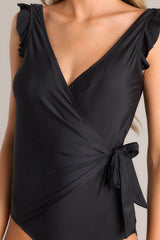 Close up view of this black swimsuit that  features a deep v-neckline, a shelf bra, removable padding, ruffled shoulders, a self-tie wrap style design, and an open back.