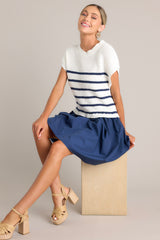 Seated full body view of this navy dress that features a crew neckline, a ribbed knitted bodice, horizontal stripes, and a solid flowy skirt.