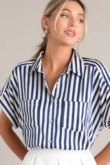 This white and blue top features a collared neckline, a full button front, functional breast pockets, a satin-like material, wide cuffed sleeves, and a split hemline.