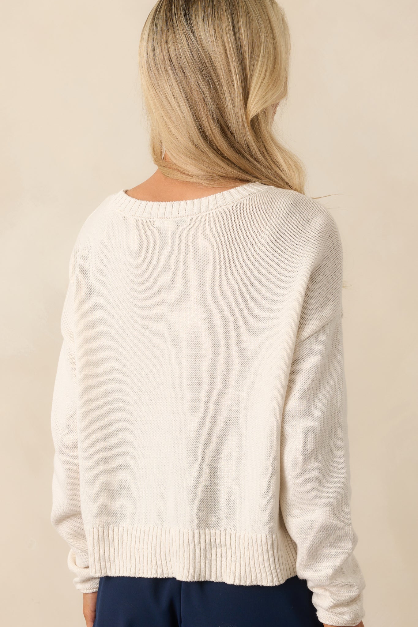 A view from behind showing the plain ivory knit, long sleeves, and relaxed fit of the sweater.