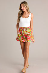 Full body view of these coral tropical print shorts that feature a high waisted design, an elastic waistband, a self-tie drawstring, functional hip pockets, and a wide leg.
