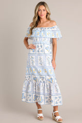 Front view of this white & blue maxi dress that features an elastic off-the-shoulder neckline, a frilled overlay that forms a false sleeve, an elastic stretch waist, an embroidered floral design, and a lined and tiered skirt.