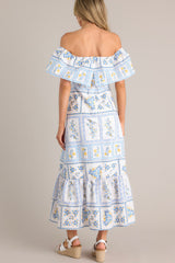Back view of this white & blue maxi dress with an elastic off-the-shoulder neckline, a frilled overlay that forms a false sleeve, an elastic stretch waist, an embroidered floral design, and a lined and tiered skirt.