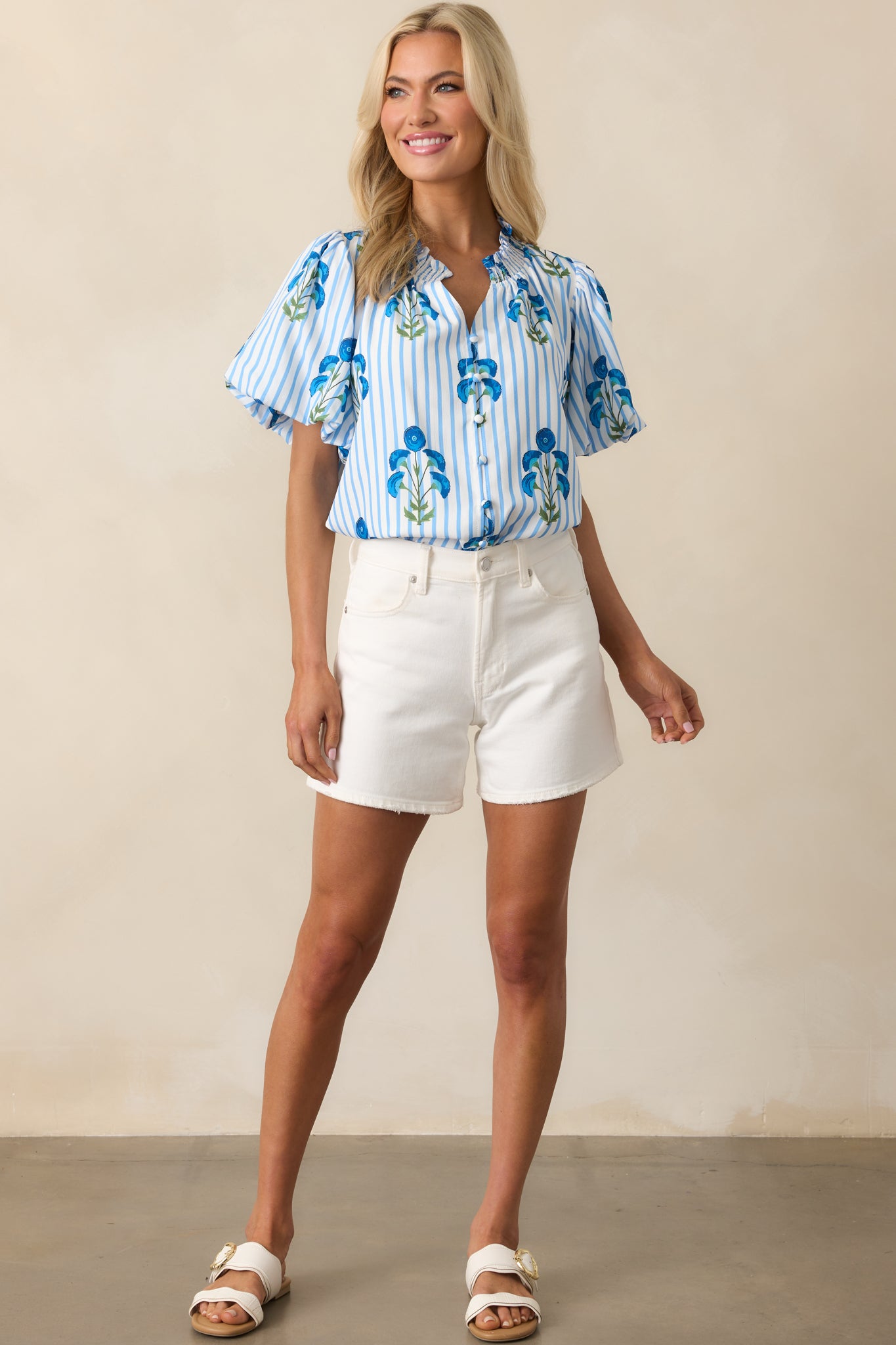 A stylish blue blouse with a button front, puff sleeves, and a ruffle v-neckline, featuring a poppy flower design that adds a touch of elegance.