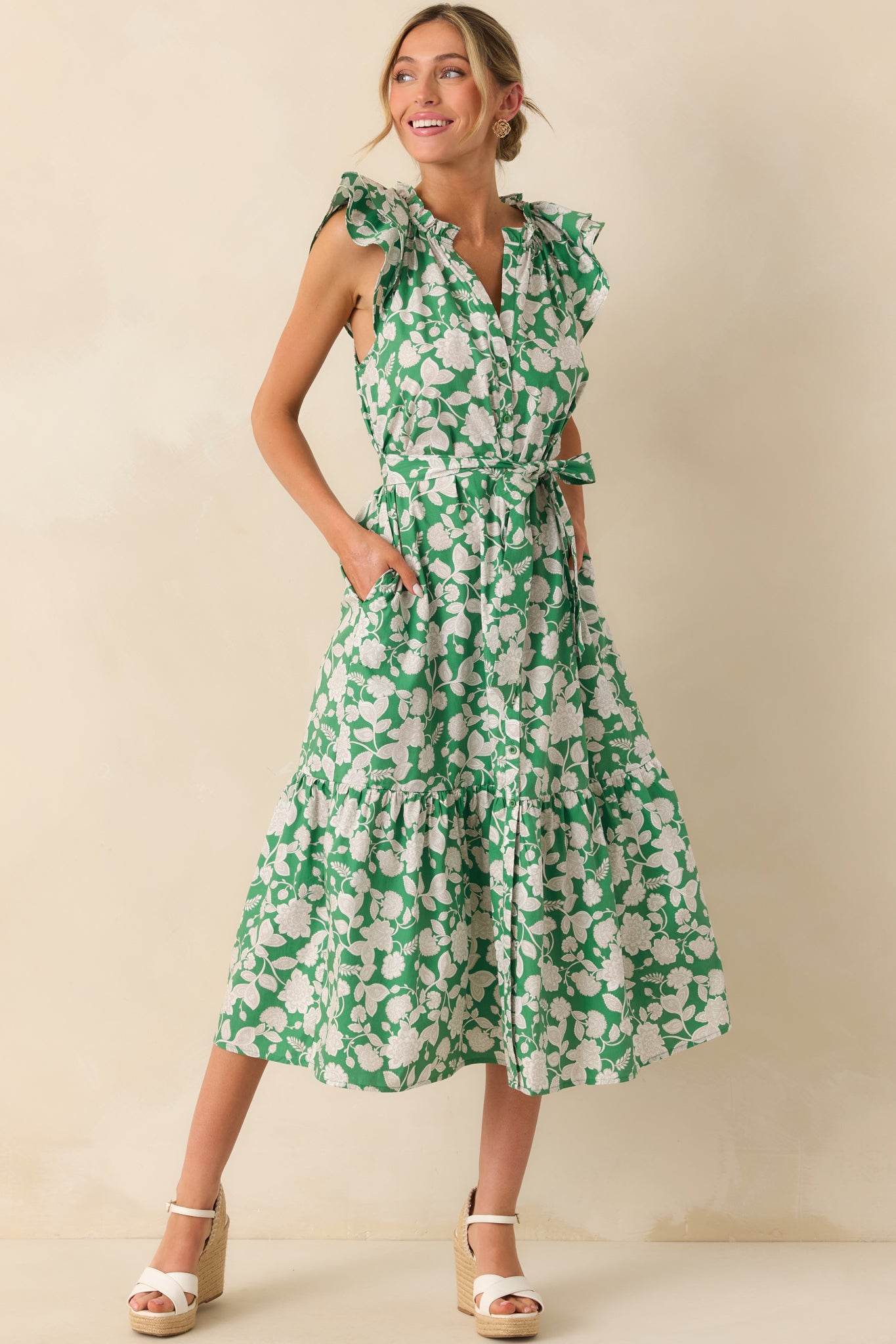 Model wearing a green maxi dress that features a ruffle notch v-neckline, layered flutter sleeves, functional button front, optional self-tie belt, 100% cotton fabric, bottom tiered skirt, and functional pockets.