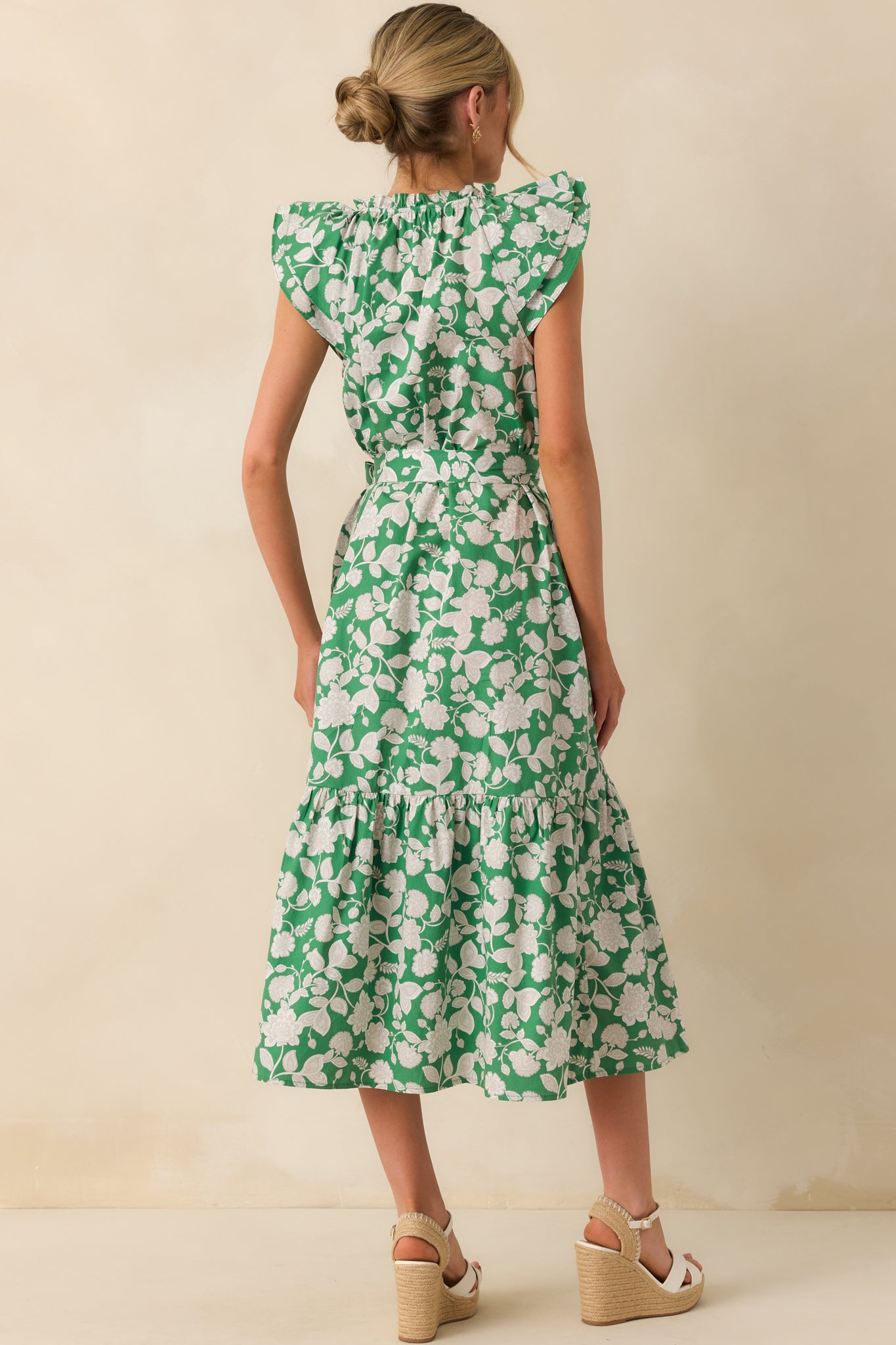 Model showing the back of a green maxi dress that features a ruffle notch v-neckline, layered flutter sleeves, functional button front, optional self-tie belt, 100% cotton fabric, bottom tiered skirt, and functional pockets.