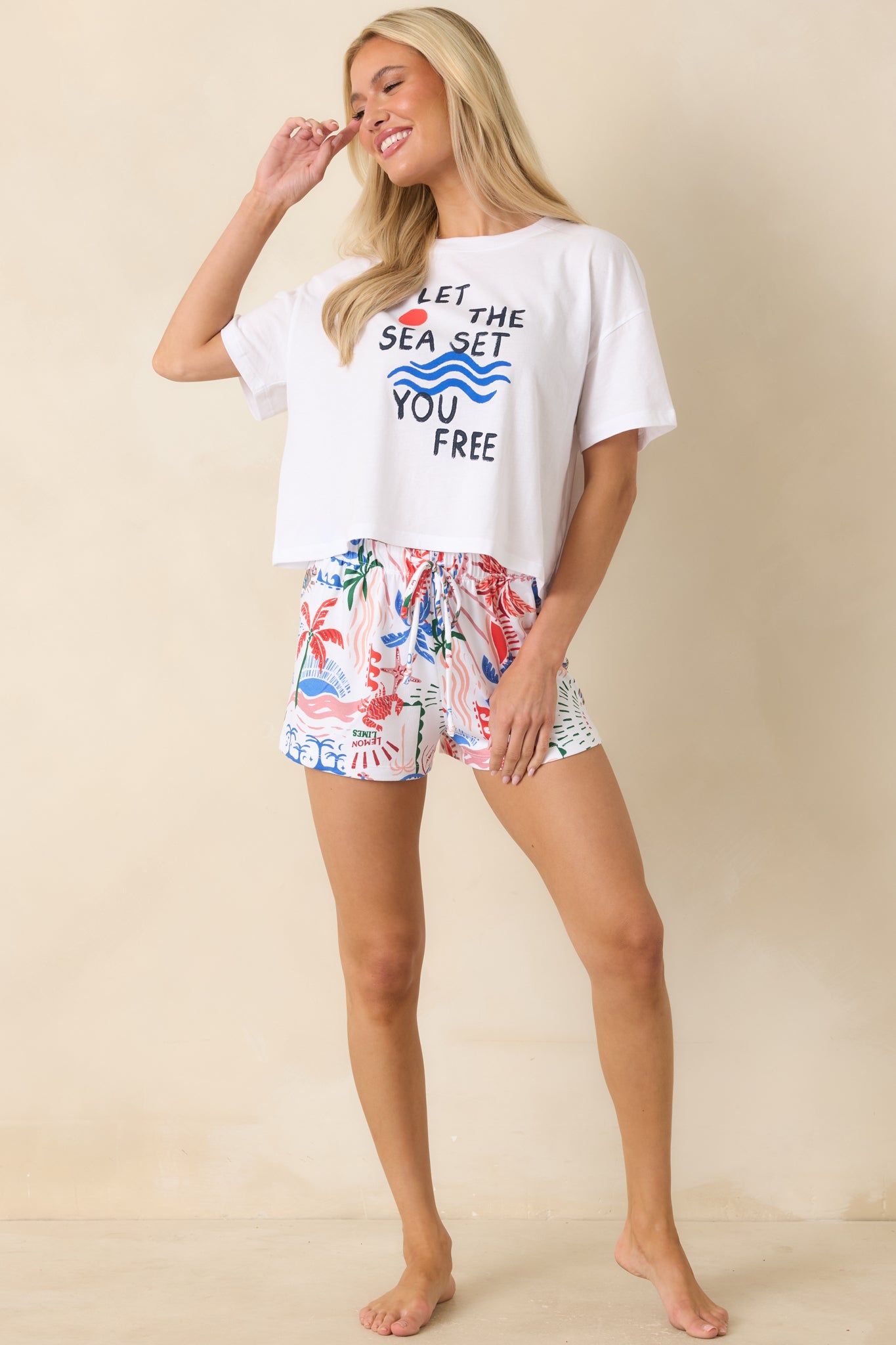 White pajama shorts featuring a colorful getaway-inspired print with tropical motifs, seashells, palm trees, waves, and citrus details across a relaxed silhouette.