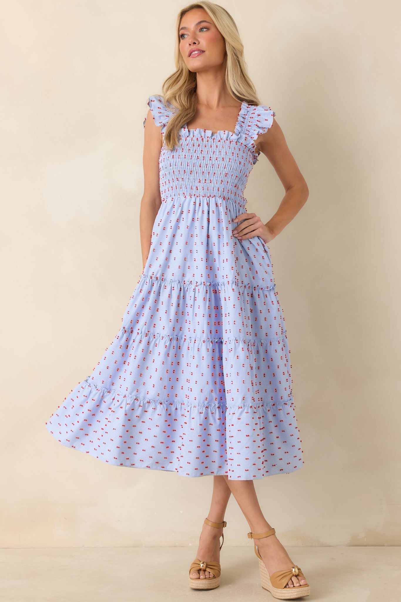 Blue gingham midi dress with a stretchy smocked bodice, tiered midi-length skirt, and vibrant red embroidered detailing throughout.