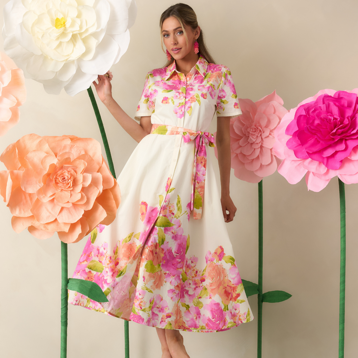 Woman in a floral dress standing among large flowers against a beige background