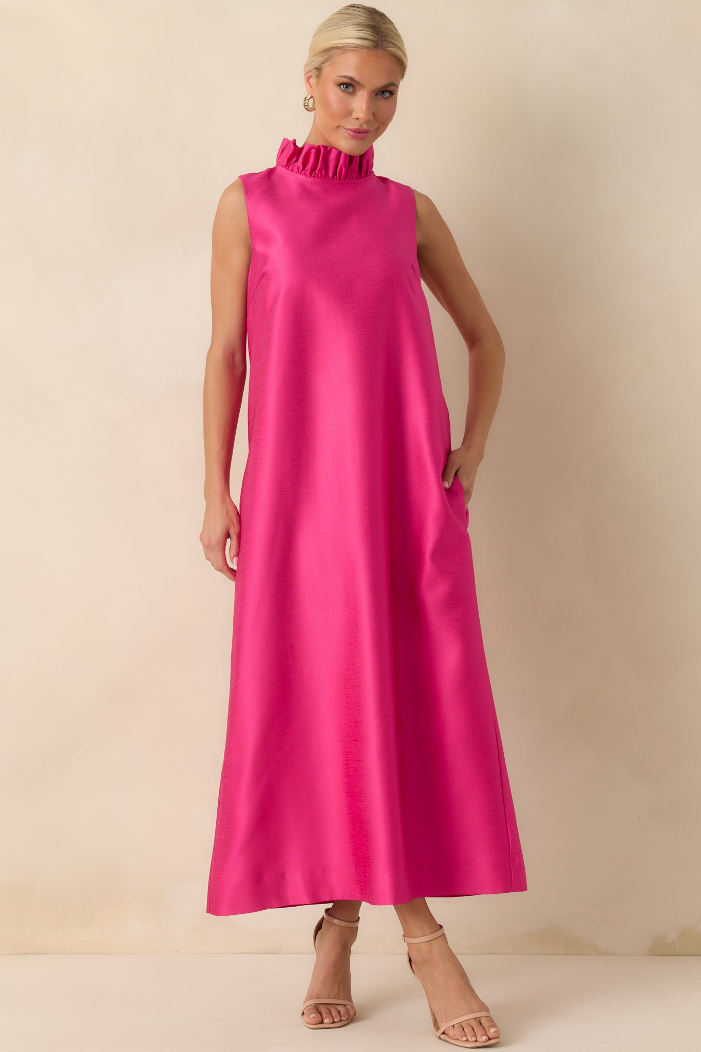 Hot pink maxi dress highlighting a straight drape, flowing fabric, and sleeveless style with ruffle neckline detail.