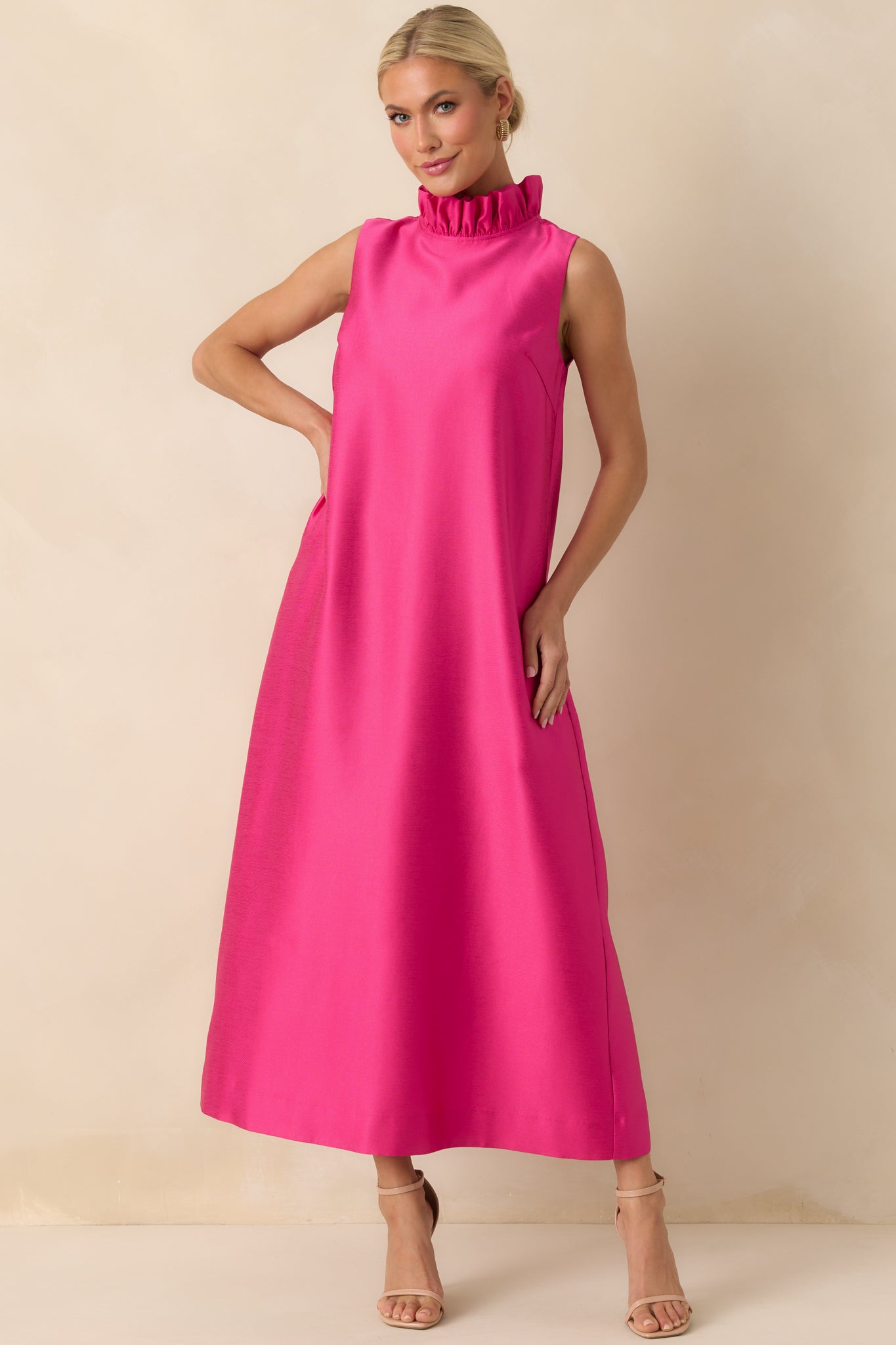 Sleeveless hot pink dress featuring a smooth fabric, maxi-length skirt, and ruffled mock neckline.
