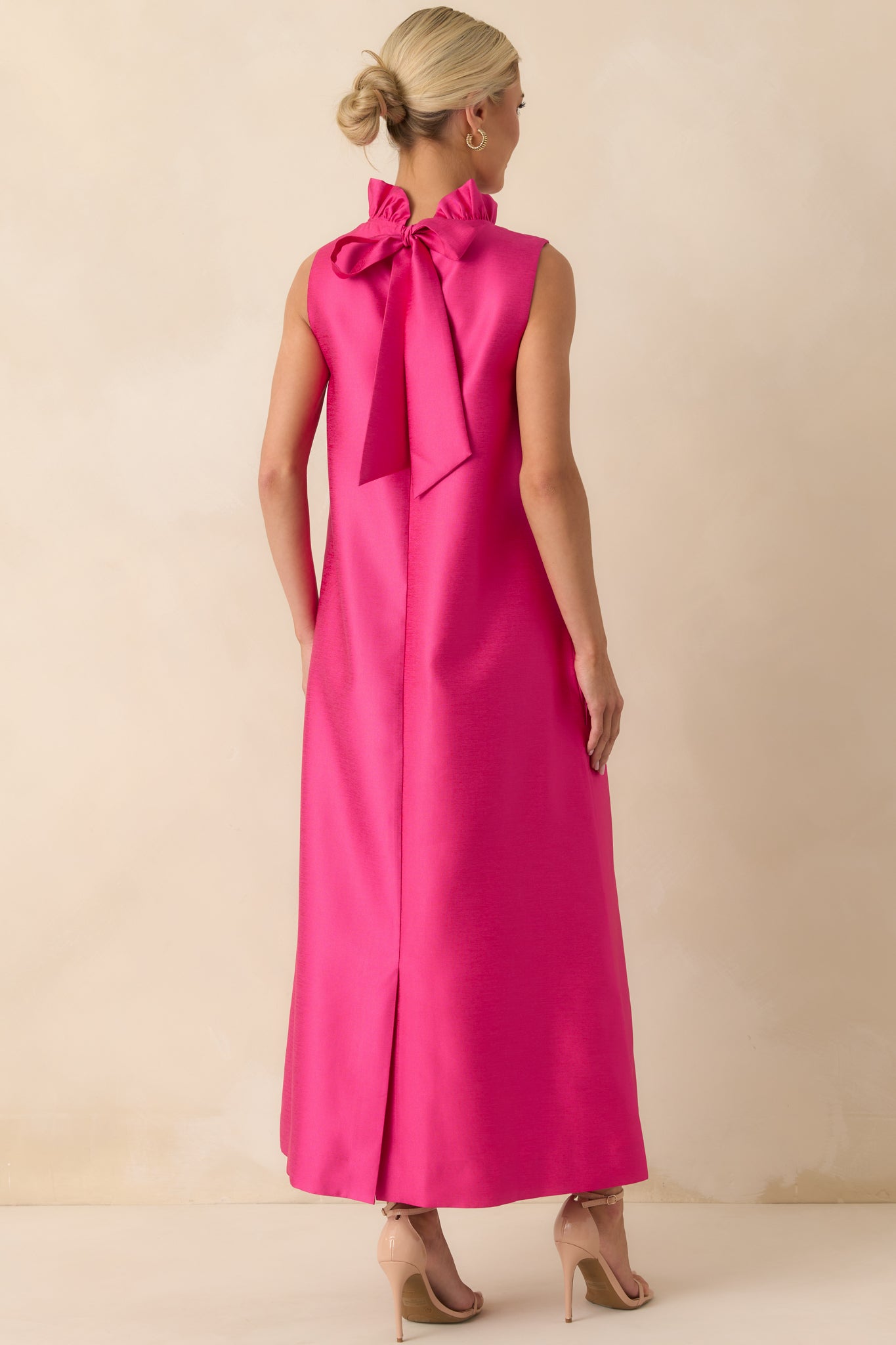 Rear view of the hot pink maxi dress displaying the back bow tie detail and flowing straight silhouette.
