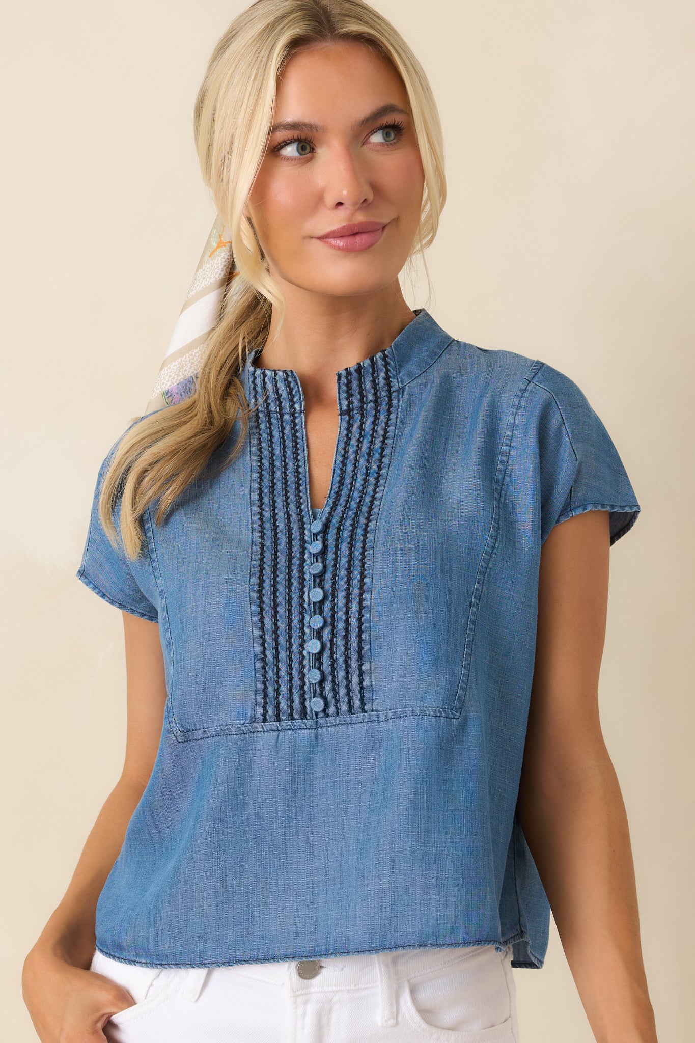 Blue top featuring a split neckline and detailed pintuck embroidery with a soft, flowing drape.