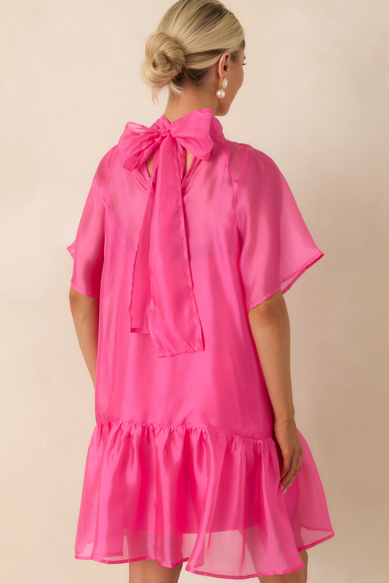 Rear view of the pink organza mini dress featuring a self-tie bow closure at the neckline, sheer sleeves, and relaxed silhouette.
