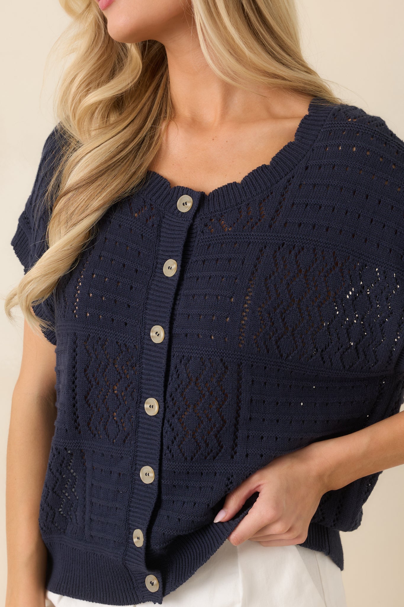 Close-up of open-knit fabric showing airy texture and soft ribbed hem and sleeve trim.