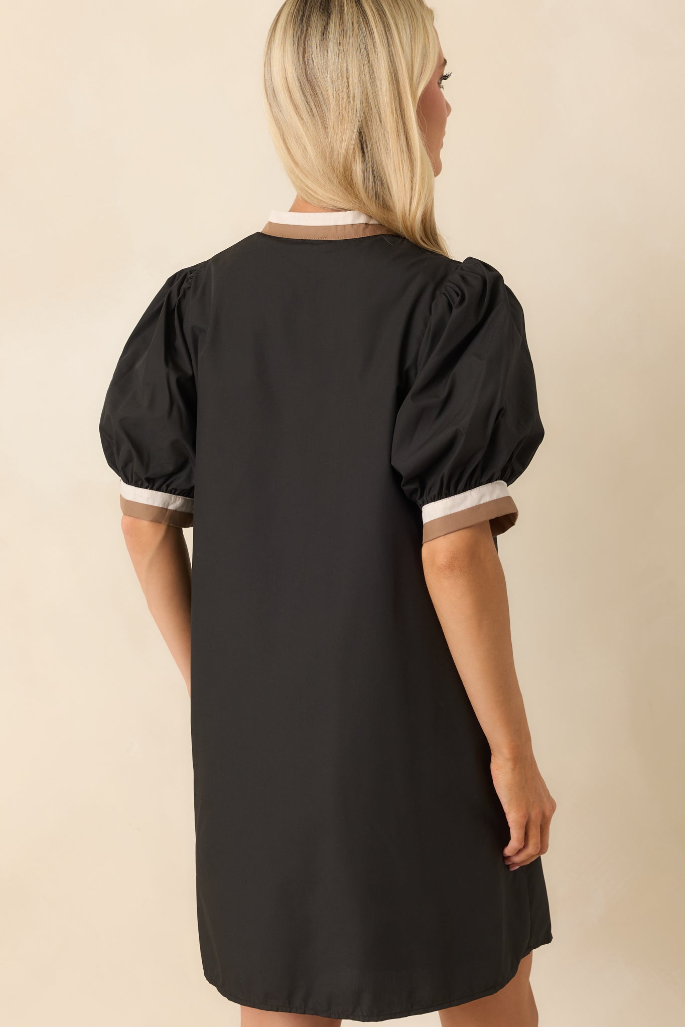 A back view of the dress showing the smooth black fabric, puff sleeve structure, and trim accents.