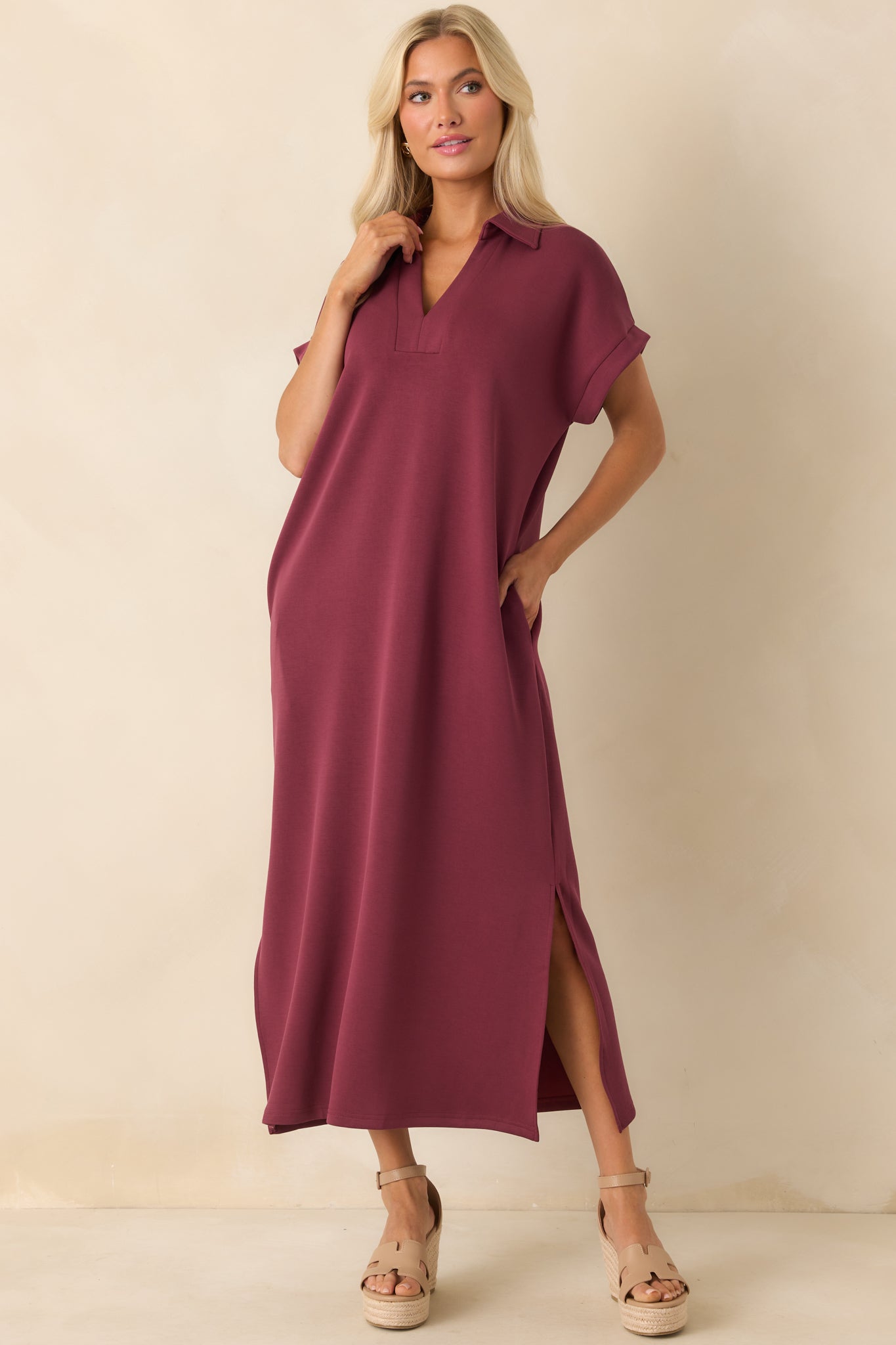 Burgundy midi dress shown from the front, featuring soft drape, side vent slits, and functional pockets.