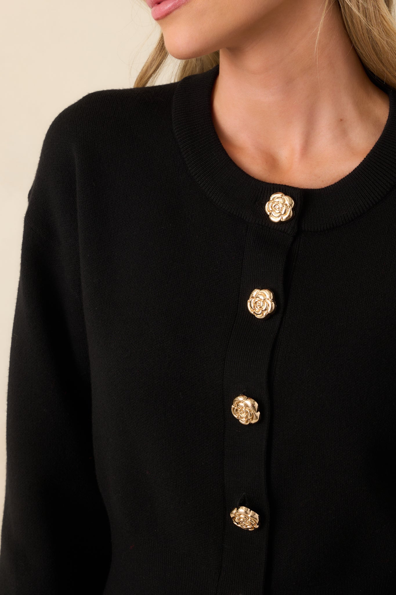 Zoomed-in image of one gold flower-shaped button on the hunter green knit fabric, showing the button’s design and textured ribbing.
