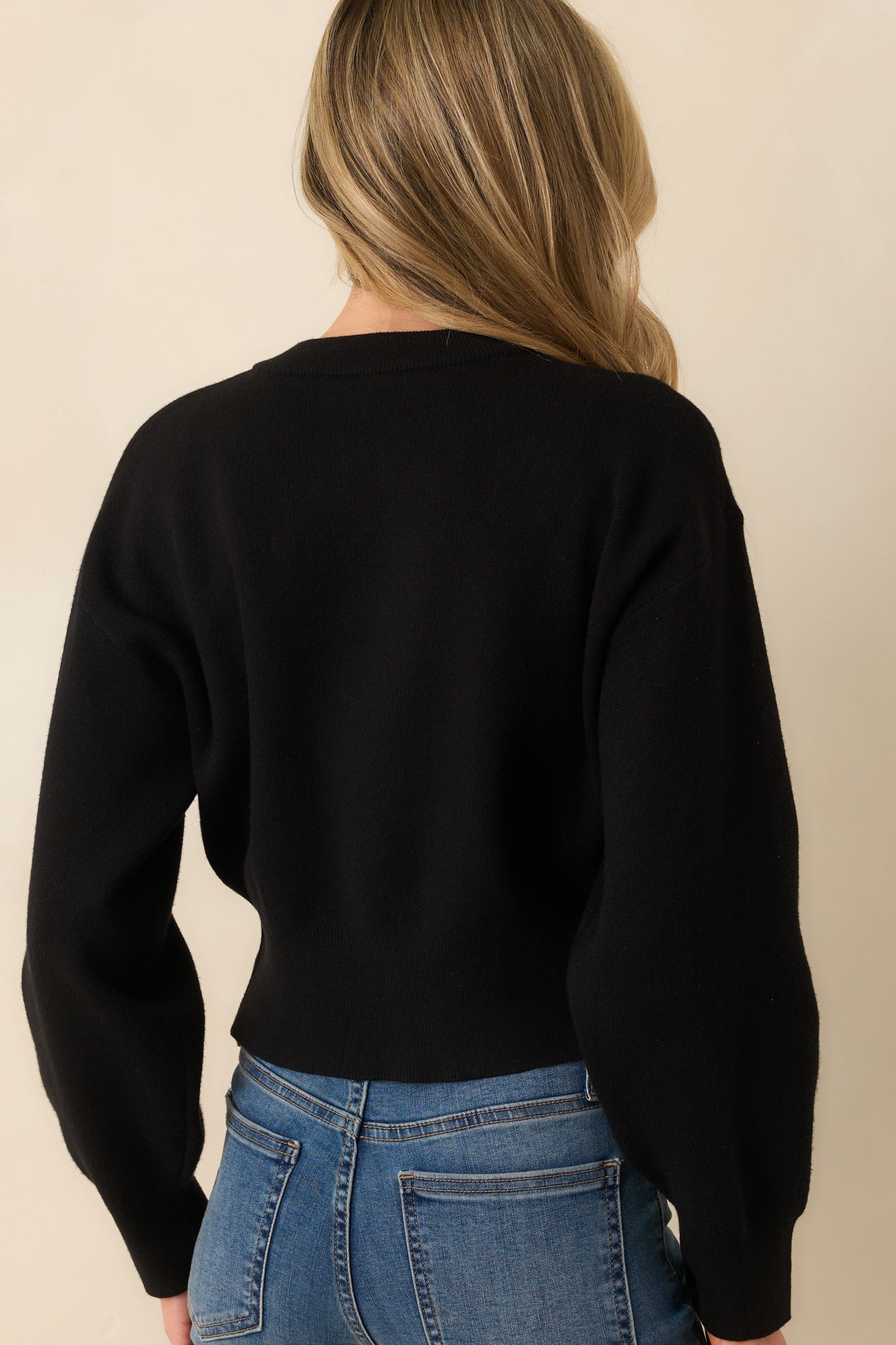 A view from behind of the black cardigan, highlighting the smooth knit fabric, long sleeves, and ribbed waistband.