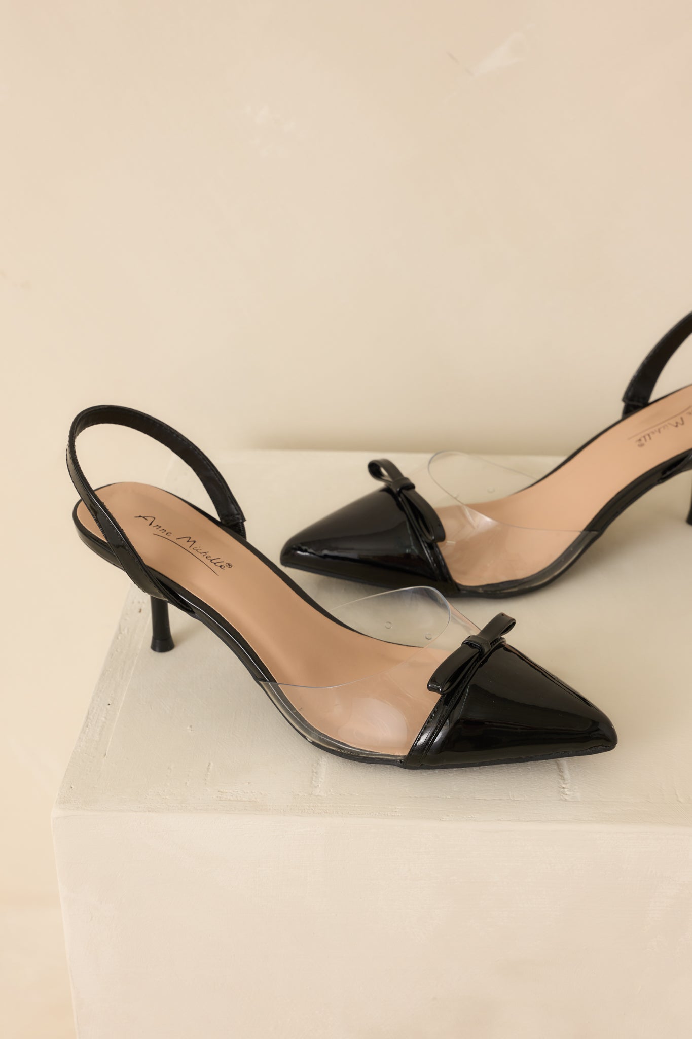 Front view of the black kitten heels against a beige background showing the pointed toe shape.