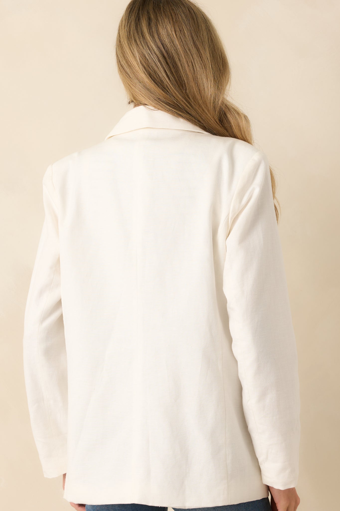 A back view of the white blazer with padded shoulders and long sleeves.