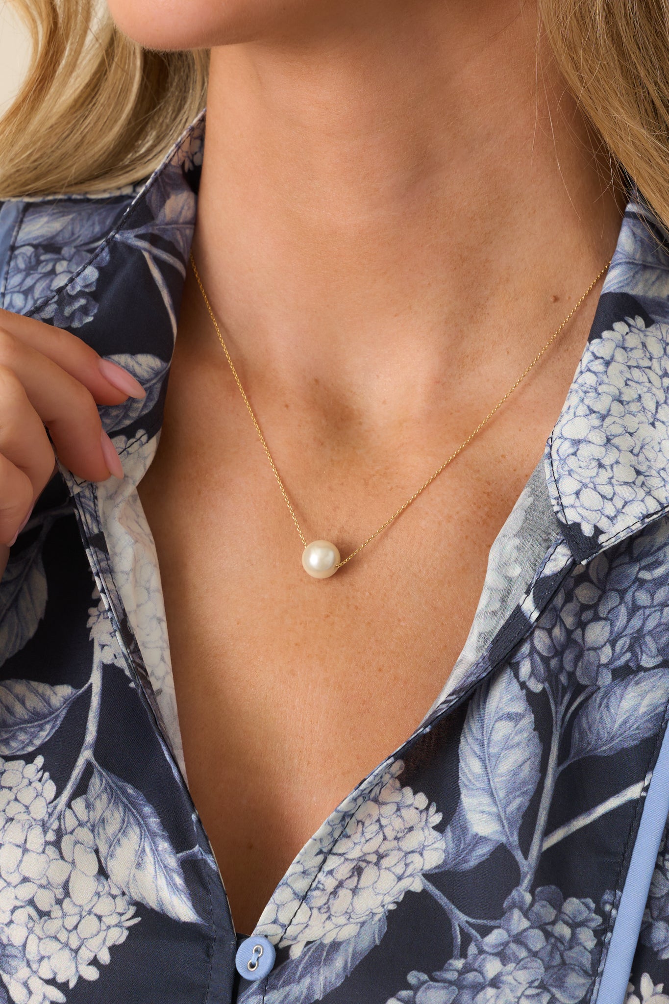 A close-up shot of the necklace being worn, showcasing its thin gold chain and ivory faux pearl pendant. 