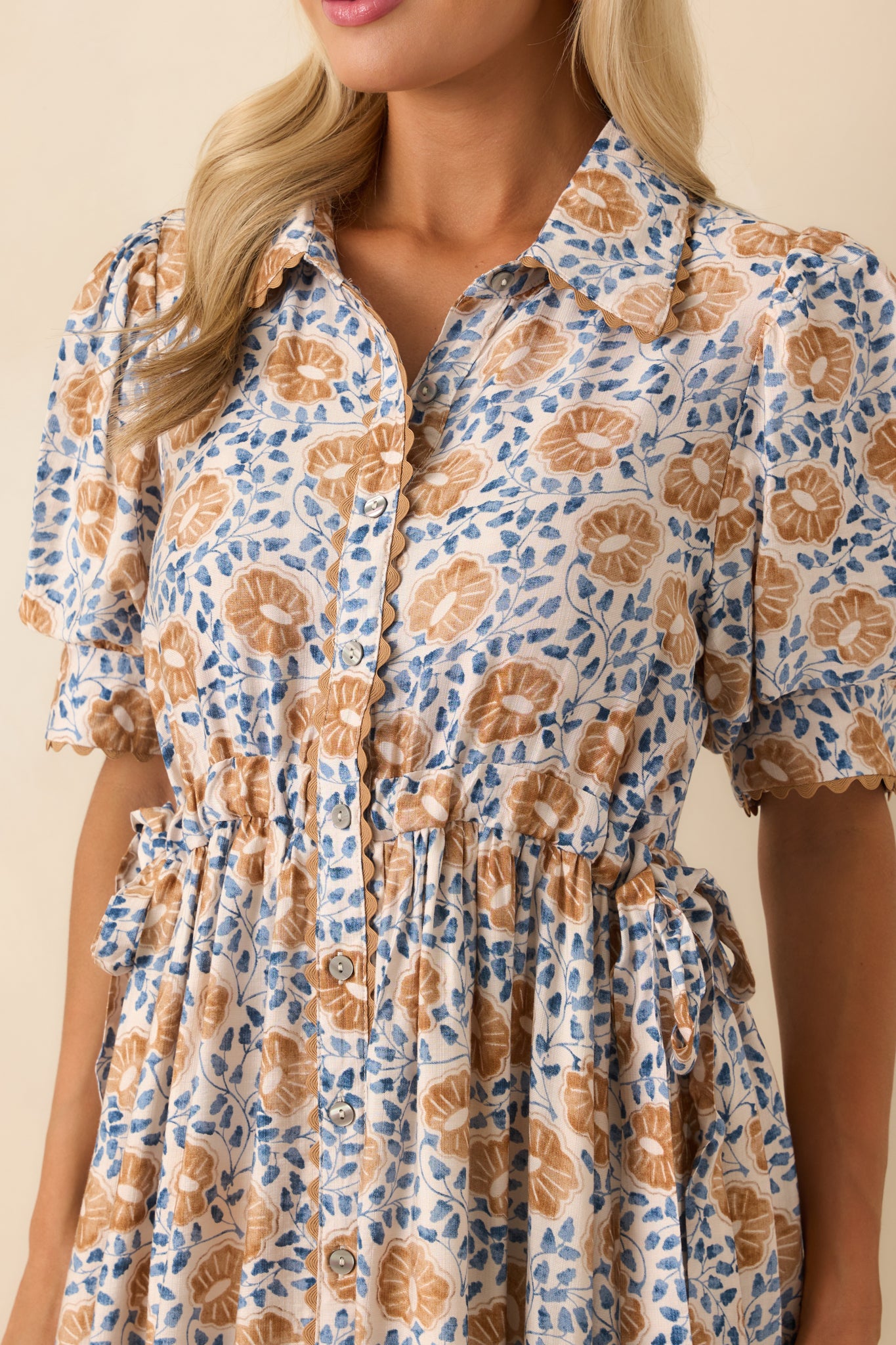 Close-up of the floral fabric and ric rac scallop trim along the neckline and button placket, showing fine detail and texture.