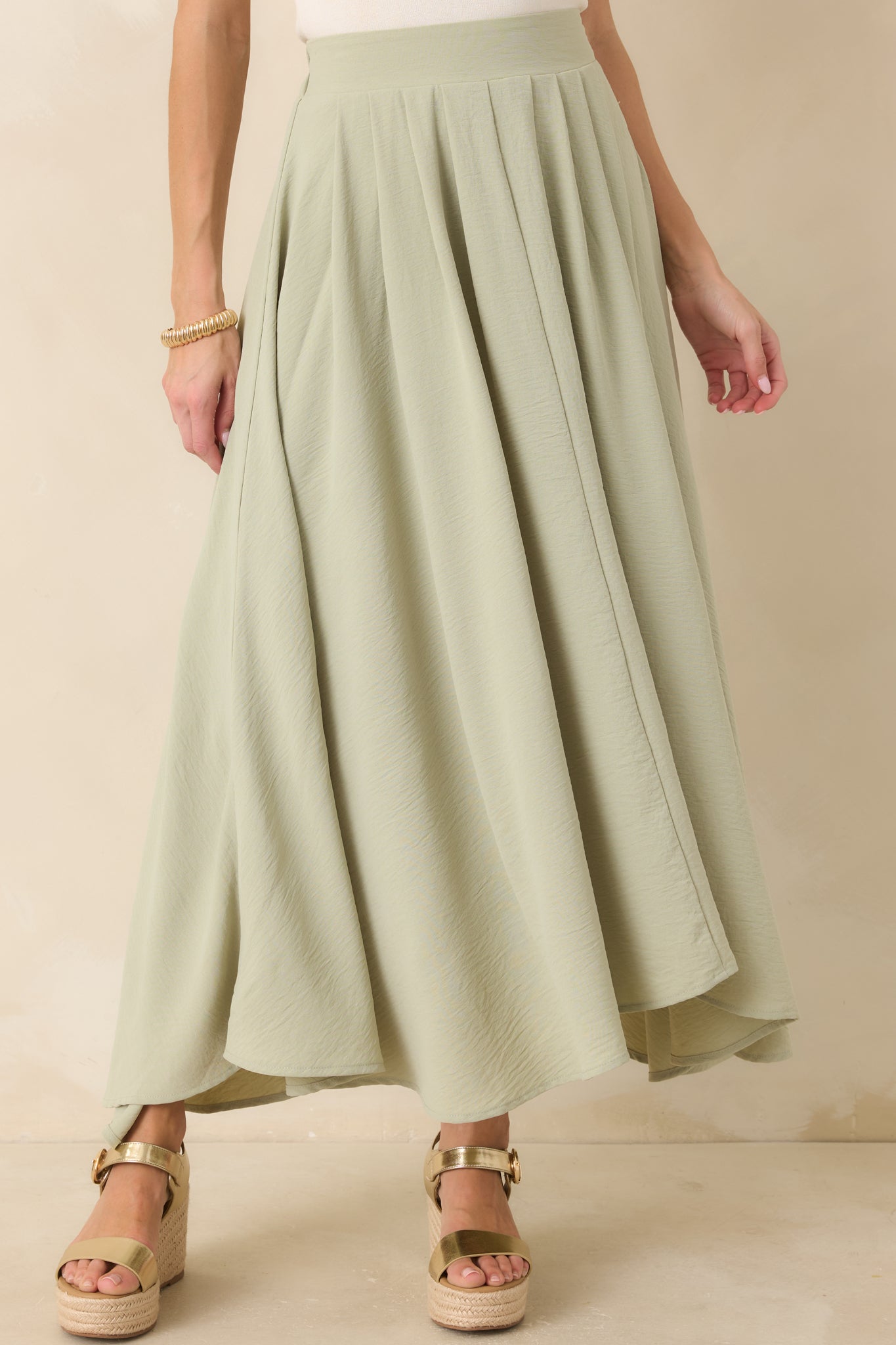 Curved hemline detail on sage green maxi skirt showing fluid drape.