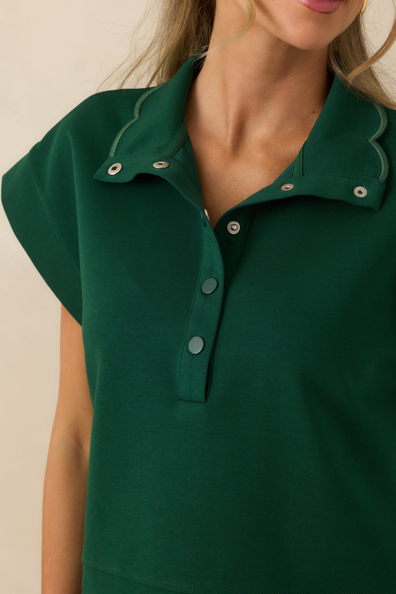 Detailed look at the embroidered scallop hem and stitching on the hunter green pullover.