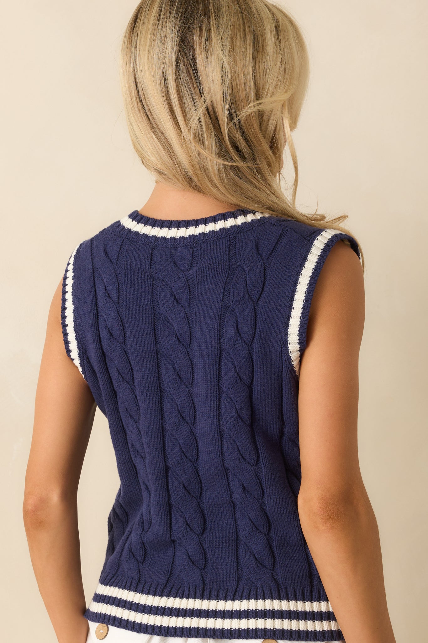 Rear view of the navy vest showing the full cable knit design and white trim along the neckline and armholes.