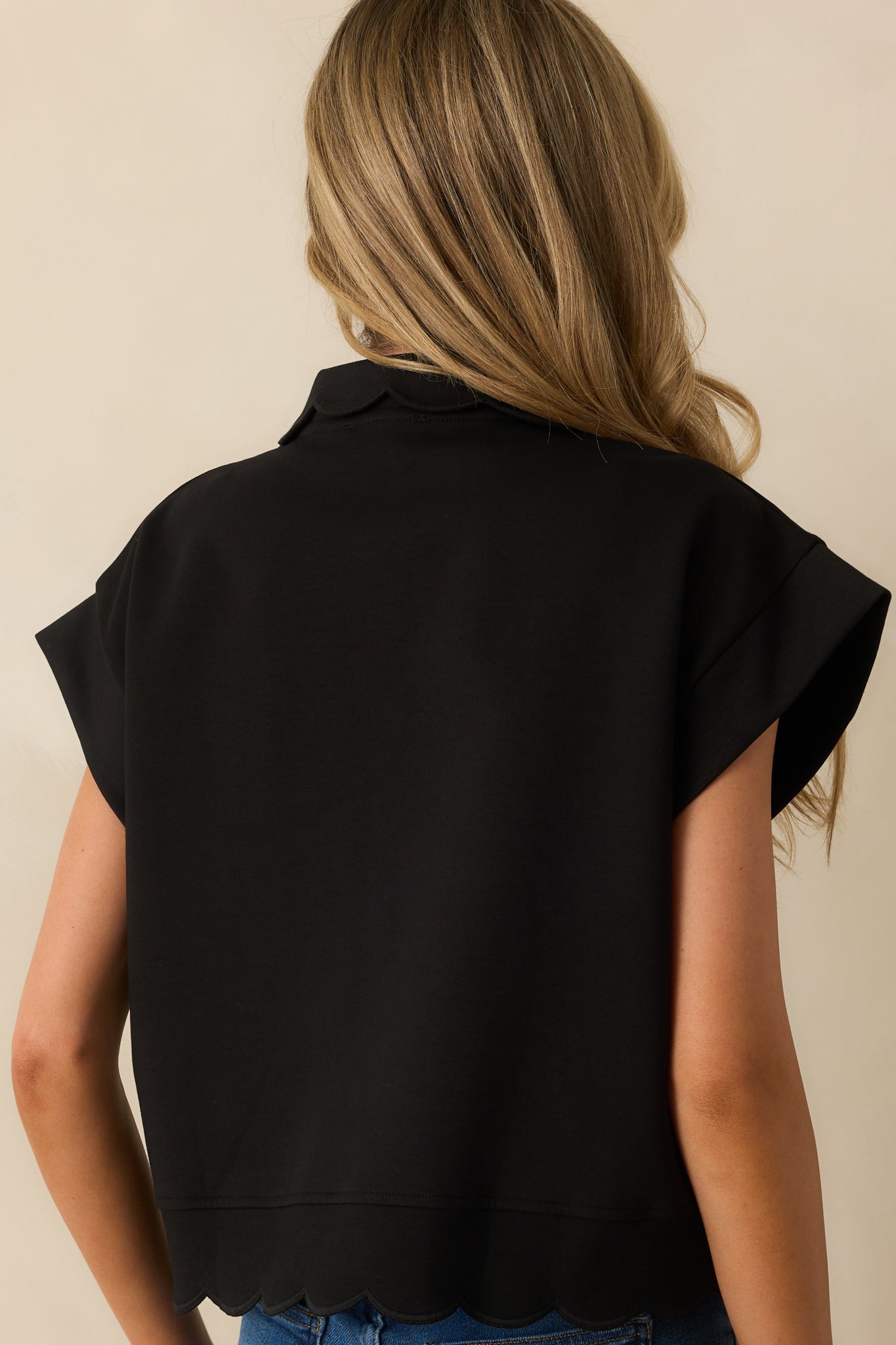 A back view of the black pullover featuring the relaxed fit and scalloped hem detail along the back hemline.
