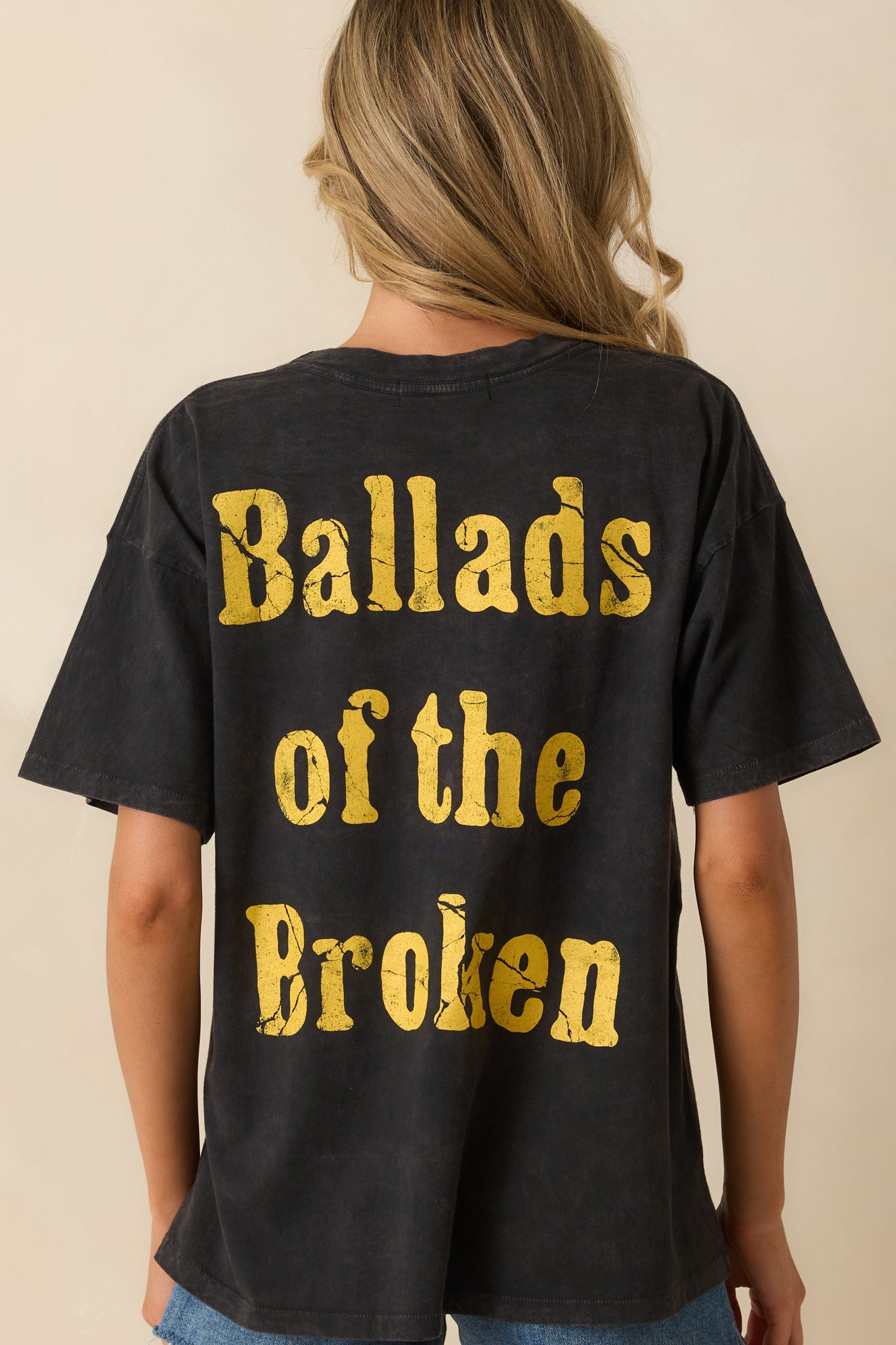 A back view of the tee featuring "Ballads of the Broken" written in yellow textured letters.