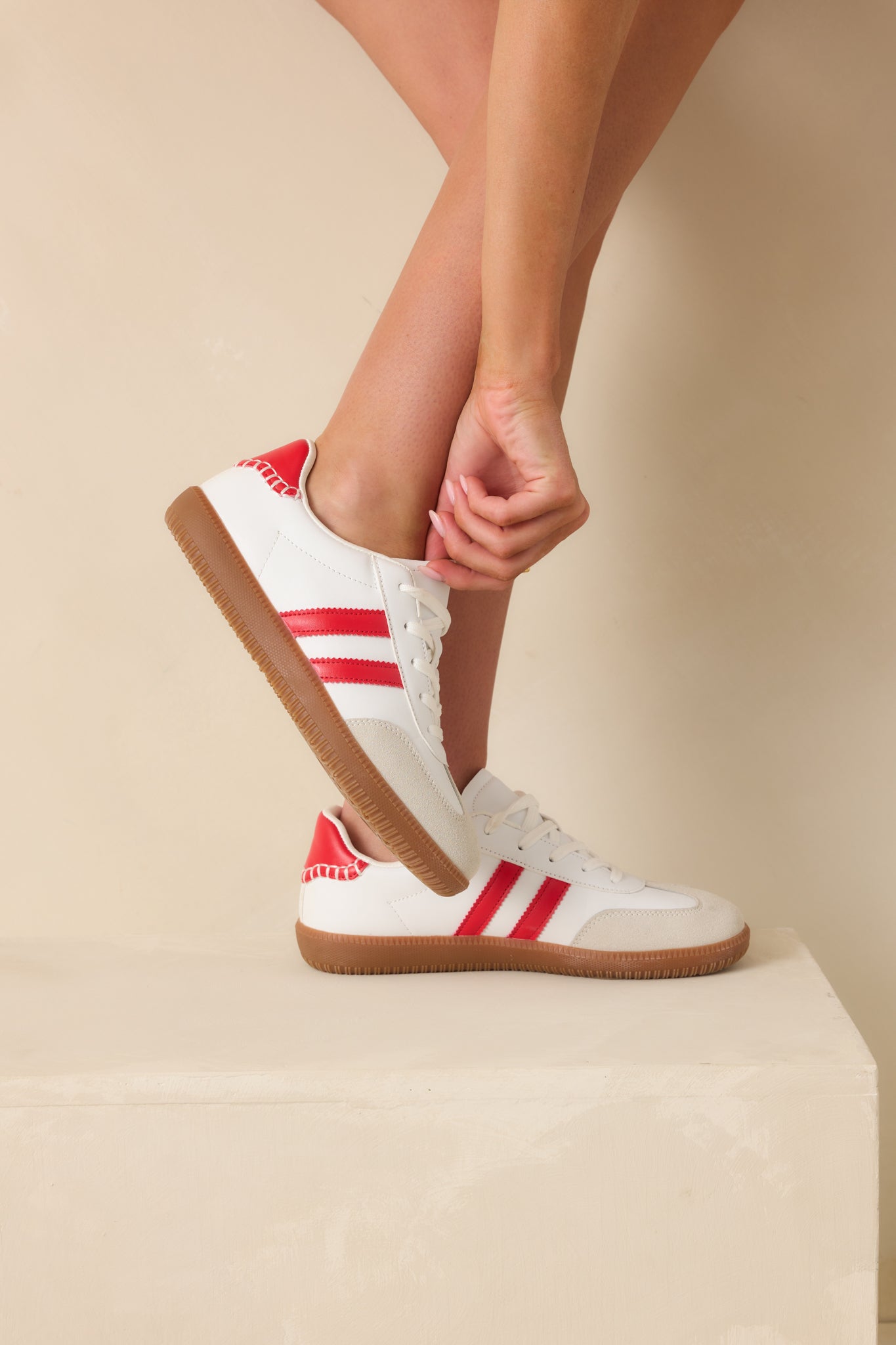 White faux leather sneakers shown from the side, highlighting the bold red ankle accent.