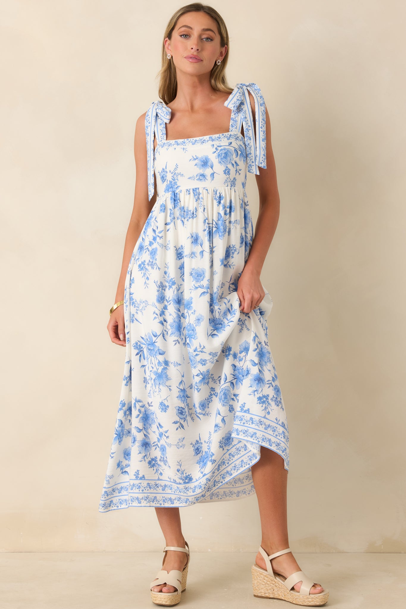 Floral maxi dress in ivory and blue with a smocked rear panel, flowing gathered skirt, delicate tie straps, and a detailed border print finish.