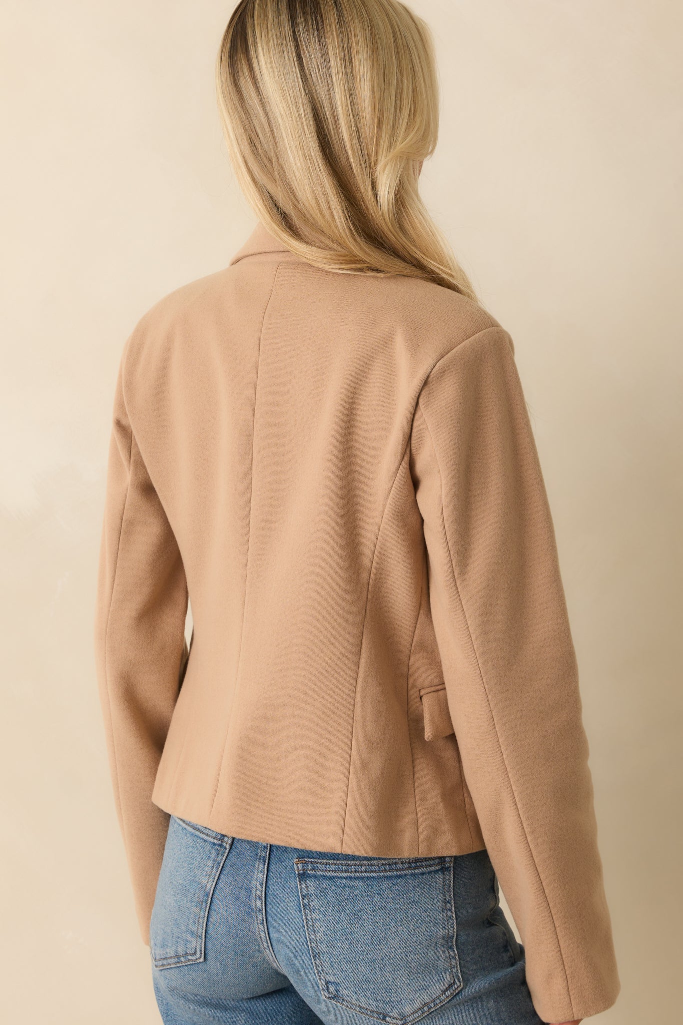 A back view of the tan blazer displaying a straight hem, long sleeves, and cropped boxy silhouette.