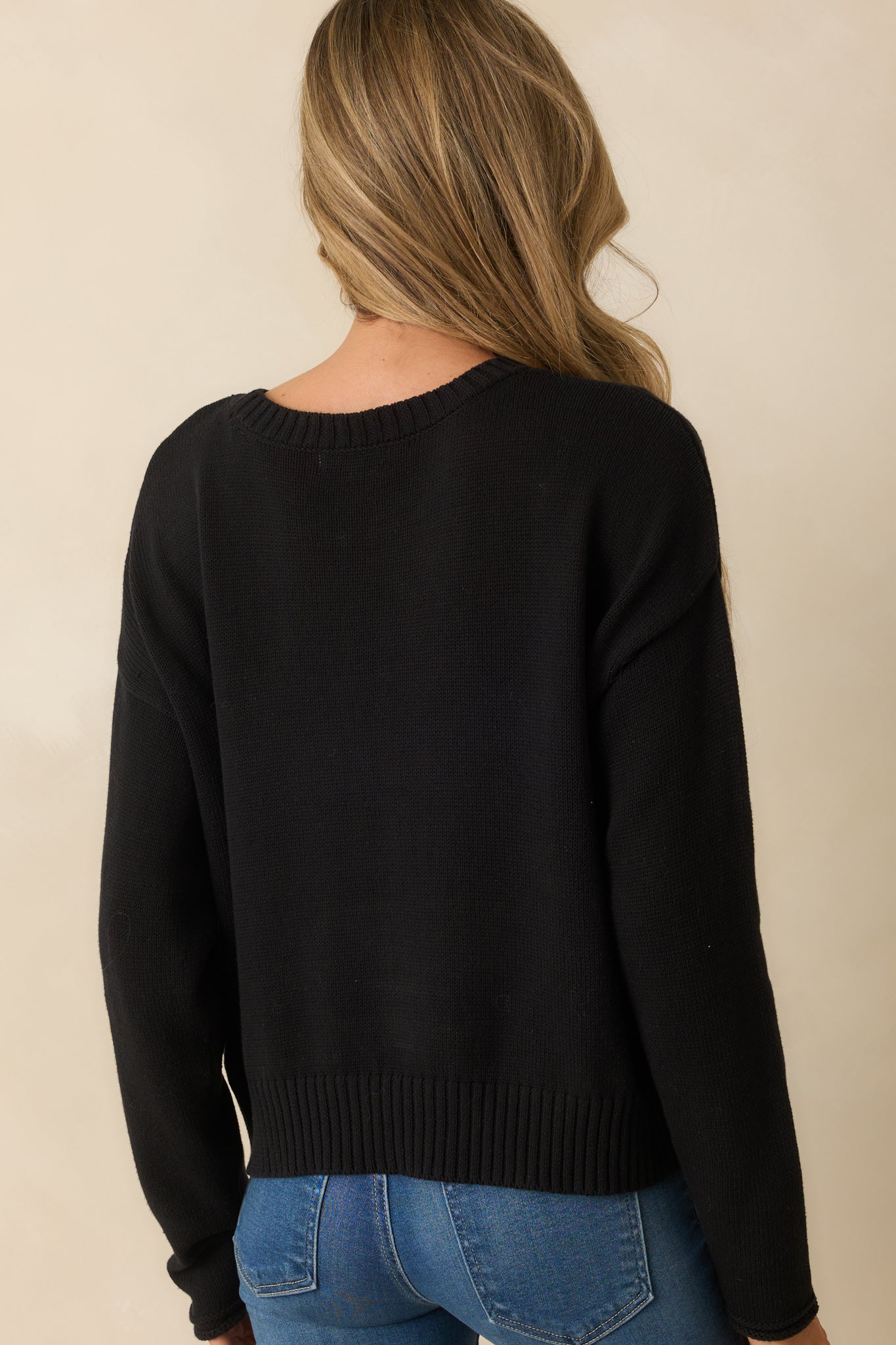 Rear view of the sweater showing solid black knit with ribbed trim.