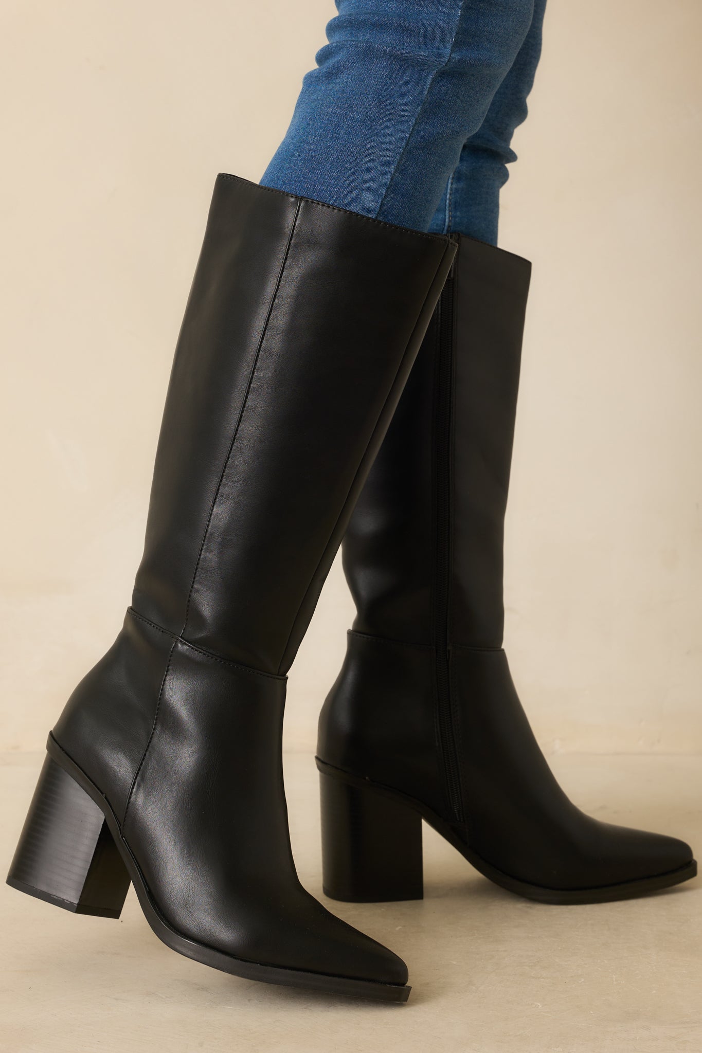 Black faux leather boots with pointed toes, side zipper closure, and paneled design, shown from a close front angle.
