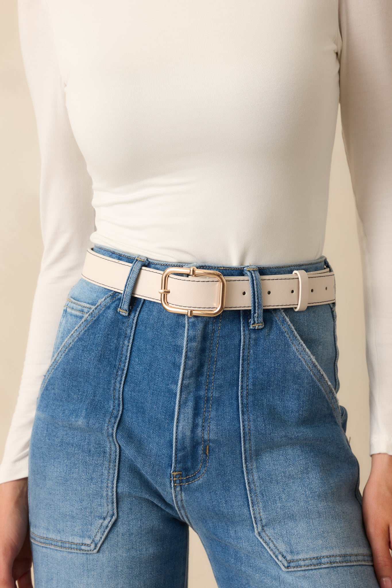 Cropped front view of the ivory belt featuring a gold square pin buckle and stitched border detail.