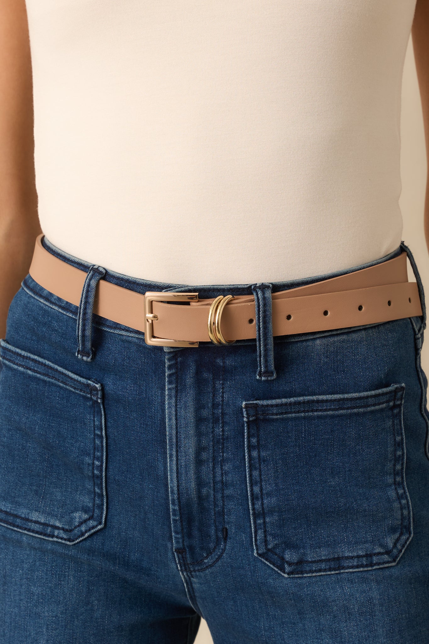 Close-up of gold-tone square buckle and double metal loop on beige faux leather strap.