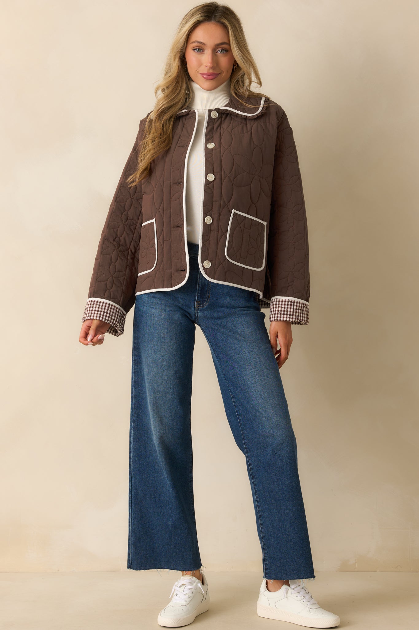 Brown quilted jacket with collared neckline, subtle ruffle trim, button front closure, and floral-patterned quilt stitching.