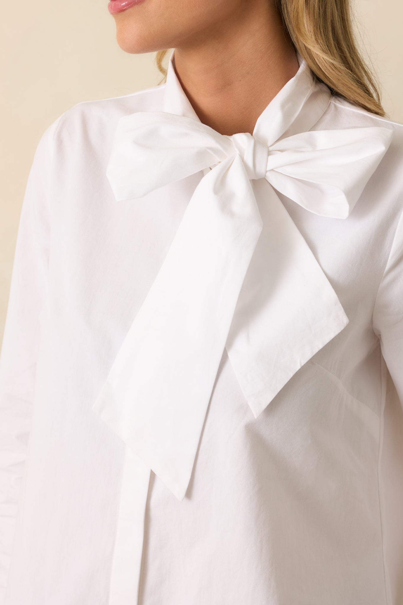 Close-up detail of the white top, emphasizing the tied bow at the neckline and front button closure.