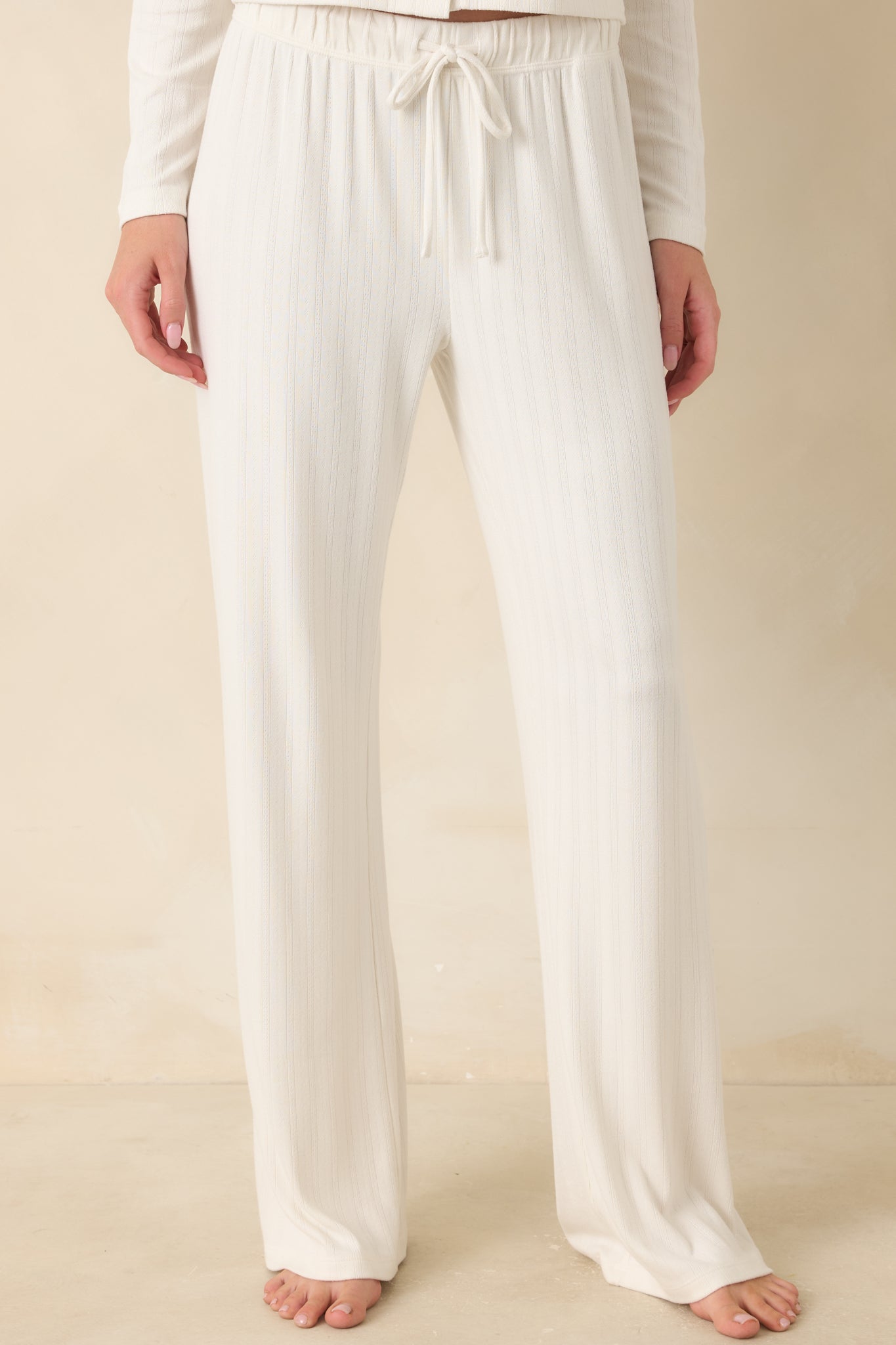 Detailed view of pointelle knit texture and drawstring elastic waistband on ivory lounge pants.